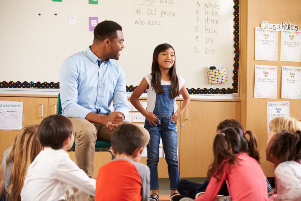 A teacher and a smiling student at the front of an elementary classroom