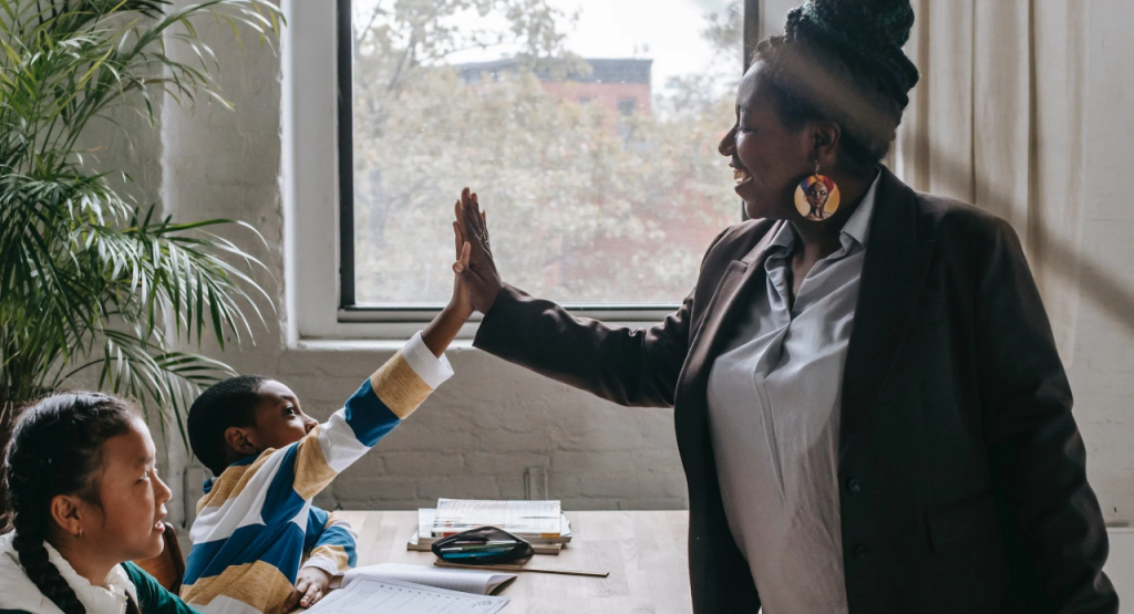 A teacher sharing a high five with a student at a classroom table